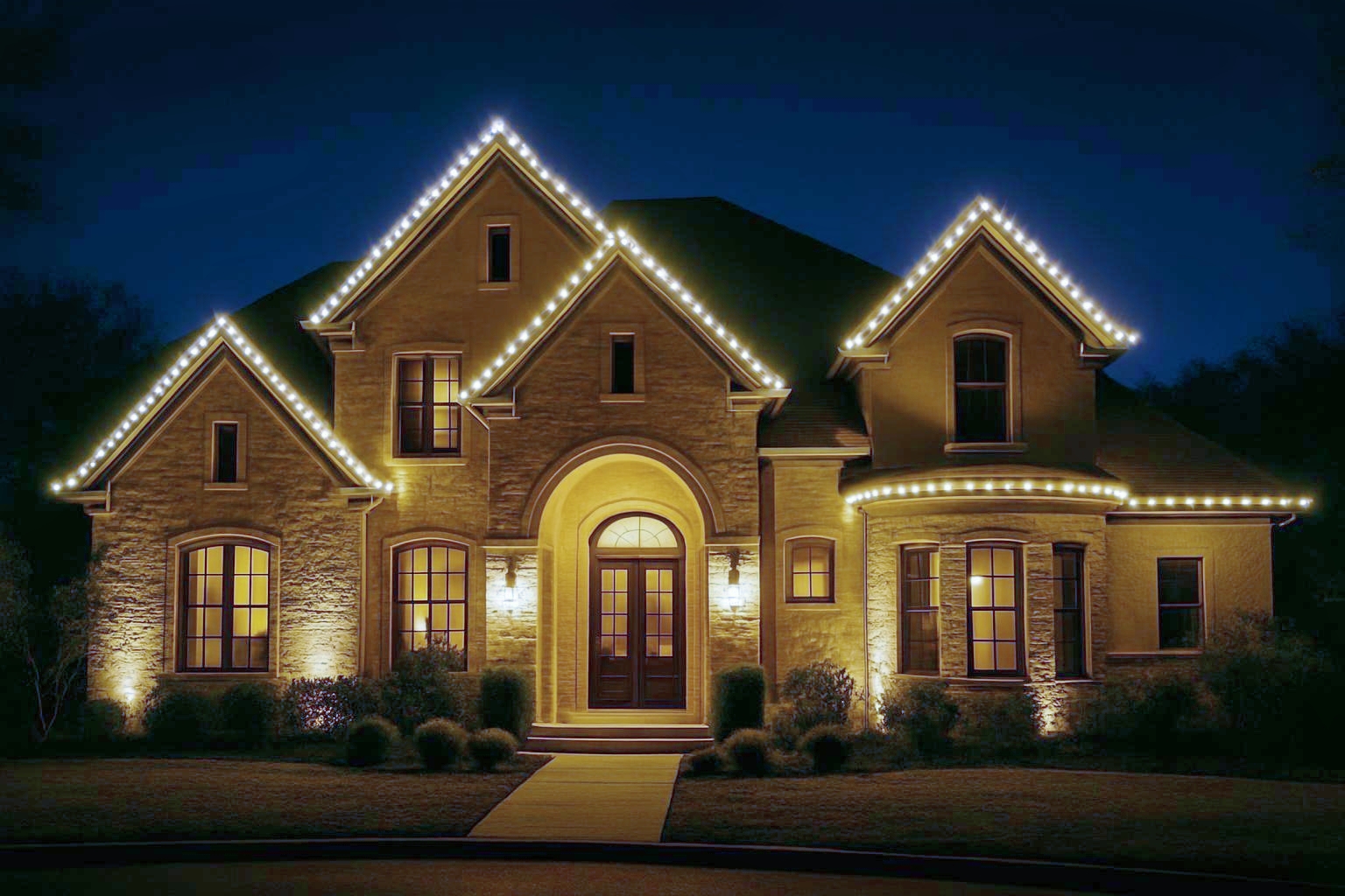 Large two-story Hill Country home beautifully decorated with warm white LED Christmas lighting, creating a cozy holiday atmosphere.